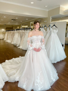 Brunette bride wears a full ballgown wedding dress with tulle and lace.  Wedding dress features a removable off the shoulder, bubble sleeve jacket